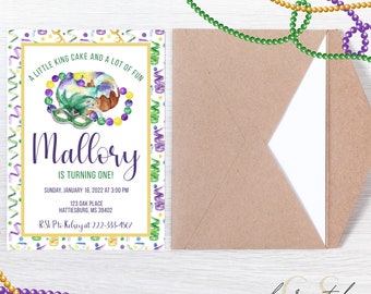 May include: A white invitation with a gold border and a colorful confetti pattern. The invitation is for a birthday party for Mallory, who is turning one. The invitation features a watercolor illustration of a king cake with purple, green, and gold beads. The text on the invitation reads "A little king cake and a lot of fun, Mallory is turning one! Sunday, January 16, 2022 at 3:00 PM, 123 Oak Place, Hattiesburg, MS 39402, RSVP to Kelsey at 222-333-4567."