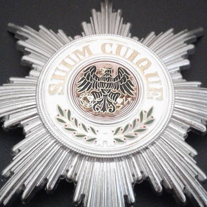 May include: A silver star-shaped medal with a central circular emblem. The emblem features an eagle design with the Latin inscription "SUUM CUIQUE". The medal has radiating rays and a detailed design.
