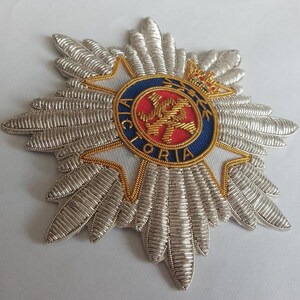 May include: A silver and gold embroidered badge with a red and blue center featuring a crown and the word "VICTORIA".