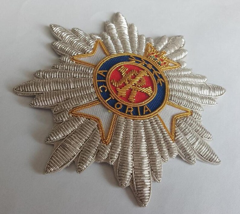 May include: A silver and gold embroidered badge with a red and blue center featuring a crown and the word "VICTORIA".