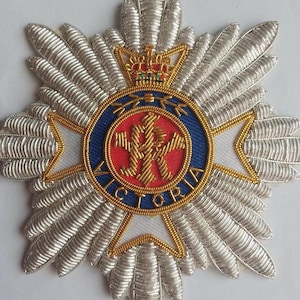 May include: A silver embroidered badge with a red and blue circle in the center. The circle has a gold crown on top and the word "VICTORIA" around the edge. The center of the circle has a gold design with a crown and the letters "VR".