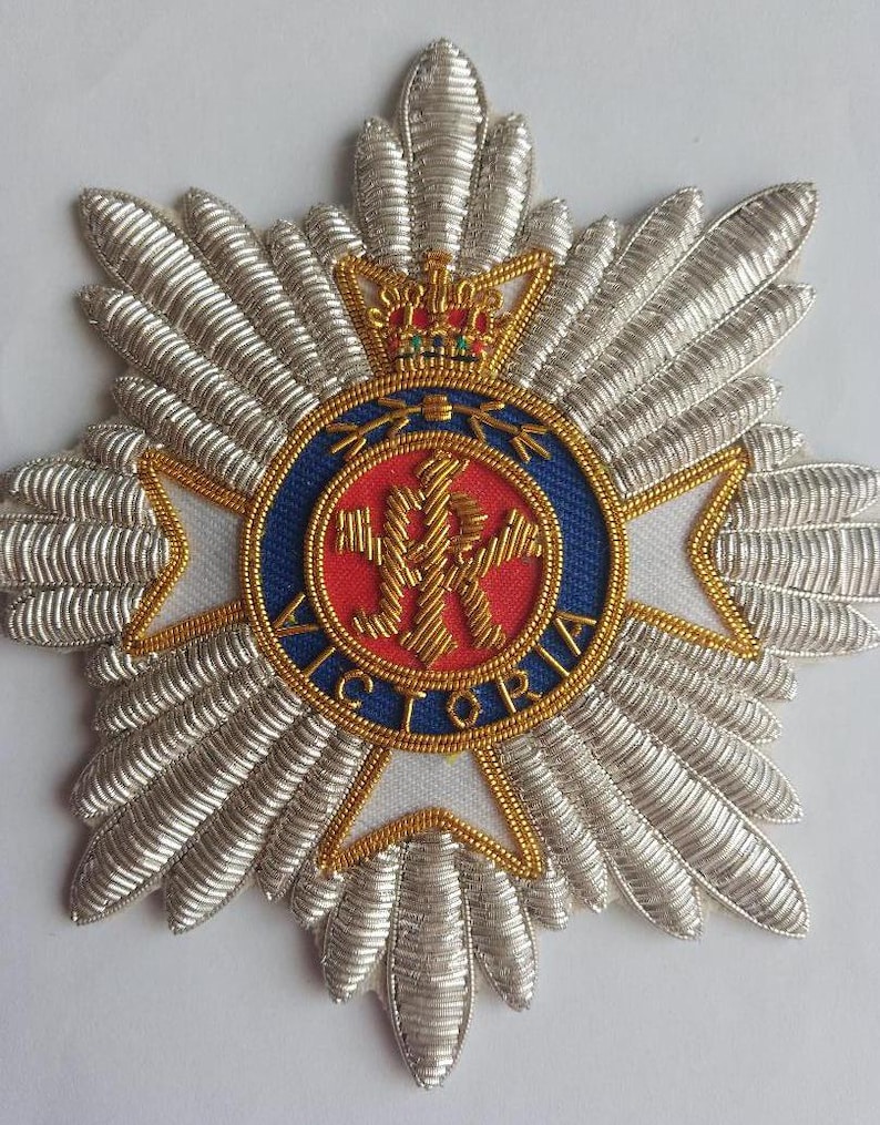 May include: A silver embroidered badge with a red and blue circle in the center. The circle has a gold crown on top and the word "VICTORIA" around the edge. The center of the circle has a gold design with a crown and the letters "VR".