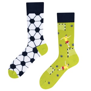 Può includere: Un paio di calzini a tema calcio. Un calzino presenta un motivo a pallone da calcio in bianco e nero. L'altro ha uno sfondo verde lime con giocatori di calcio, porte e palloni. Entrambi hanno polsini blu navy e punte verde lime.