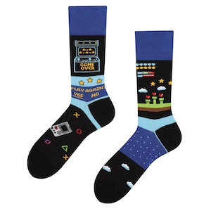 Może przedstawiać: Para czarno-niebieskich skarpet z retro wzorem gry wideo. Skarpety przedstawiają pikselową grę arcade, joystick i tekst "Game Over" oraz "Grać ponownie? Tak Nie".