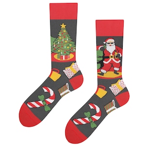 Pode incluir: Um par de meias de Natal vermelhas e pretas com um design festivo. Uma meia apresenta uma árvore de Natal com enfeites e presentes, enquanto a outra meia apresenta o Papai Noel segurando uma sacola de presentes. Ambas as meias têm bengalas de doces e caixas de presente.