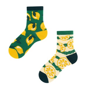Könnte beinhalten: Zwei Paar Socken mit Zitronenmuster. Ein Paar ist grün mit gelben Zitronen und das andere Paar ist weiß mit gelben Zitronen und grünen Streifen.
