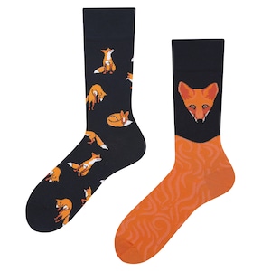 May include: A pair of socks with a fox design. One sock has a black background with orange foxes in various poses. The other sock has an orange background with a fox face.