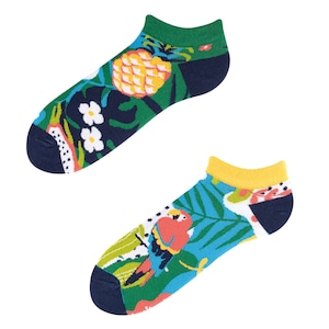 Può includere: Un paio di calzini da caviglia colorati con stampe tropicali. Un calzino presenta un ananas e dei fiori, mentre l'altro ha un tucano e foglie di palma.