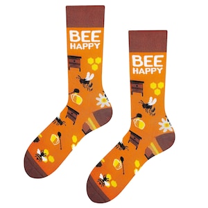 Könnte beinhalten: Ein Paar orangefarbene und braune Socken mit einem Bienen- und Wabenmuster. Die Socken haben den Text "Bee Happy" aufgedruckt.