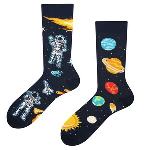 Könnte beinhalten: Ein Paar marineblaue Socken mit Weltraum-Motiv. Eine Socke zeigt Astronauten, einen Kometen und ein Space Shuttle. Die andere Socke zeigt Planeten, darunter Saturn, und eine Sonne. Die Socken sind ein lustiges Accessoire.