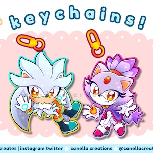 May include: Illustration of two cartoon character keychains. One is a white hedgehog with orange and teal accents, and the other is a purple cat-like character. The word "keychains!" is written above them.