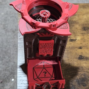 May include: A red and brown 3D printed dice tower with a question mark on the front. The tower has a flower-shaped top with a small opening for dice to fall through.