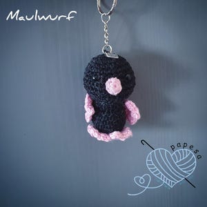 May include: Black crocheted bird keyring with pink wings and a pink nose. The keyring is attached to a silver key ring.