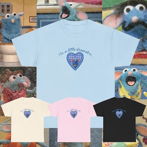 May include: A light blue t-shirt with the phrase "I'm a little dramatic" and a heart-shaped graphic featuring a cartoon character. Other t-shirts in cream, pink, and black are also displayed.