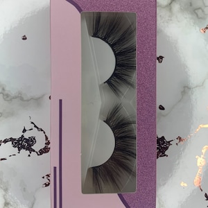May include: A pair of false eyelashes in a pink and purple box. The eyelashes are black and have a wispy, dramatic look.