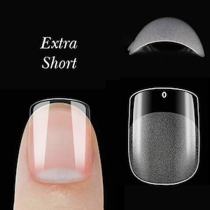 Puede incluir: Puntas de uñas de plástico transparente para aplicar uñas artificiales. Las puntas son cortas y tienen una forma ligeramente curva. El texto "Extra Short" es visible en la imagen.