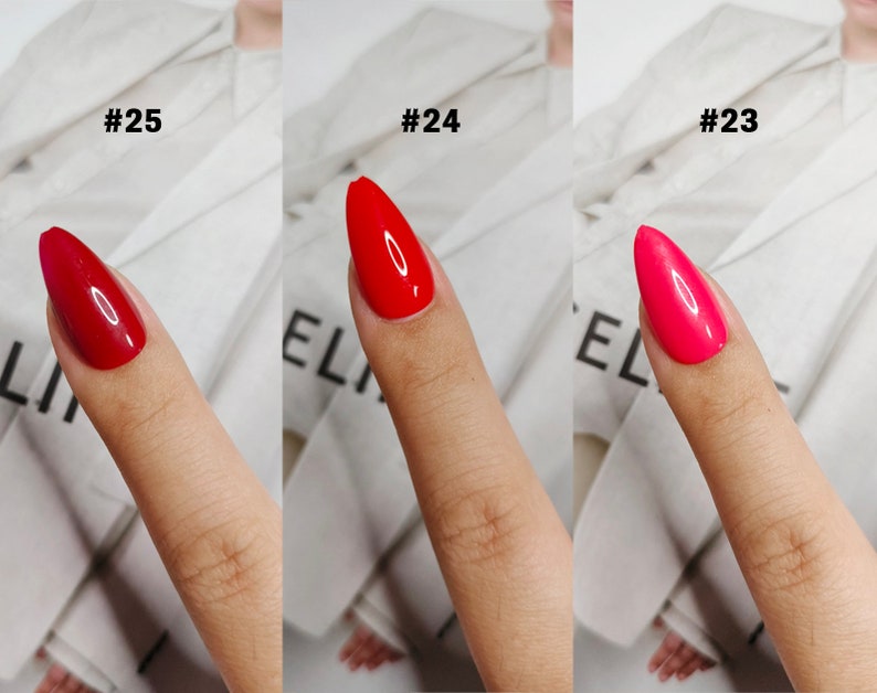 May include: Three almond-shaped fingernails with glossy polish in shades of deep red, bright red, and hot pink, labeled #25, #24, and #23 respectively. Each nail displays a smooth, reflective finish with a distinct color variation across the set.