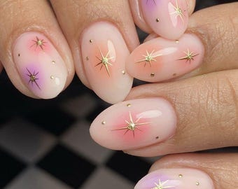 Uñas postizas acrílicas hechas a mano con diseño de estrellas doradas en tonos morado y rosa, color morado.