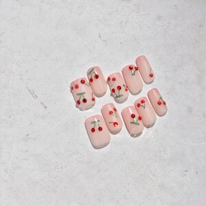 Pu&ograve; includere: Set di dieci unghie finte rosa con un design a ciliegie. Ogni unghia presenta una ciliegia rossa con un gambo e una foglia verdi. Le ciliegie sono accentate da un piccolo strass.