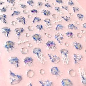 May include: A sheet of clear nail stickers with a variety of iridescent jellyfish designs. The stickers are on a pink background and feature the word "Jellyfish" printed on the sheet.