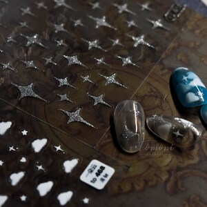 May include: A sheet of silver glitter nail art stickers with a variety of star shapes. The sheet is labeled "Tomomi Nail Art".