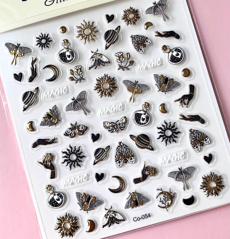 May include: A sheet of clear stickers with a variety of gold and black designs, including moons, stars, planets, butterflies, and the word "MAGIC".