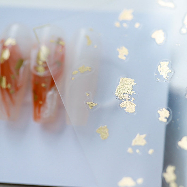 May include: A sheet of clear plastic with gold flakes scattered across the surface. The plastic sheet is slightly translucent, allowing the gold flakes to shimmer through.