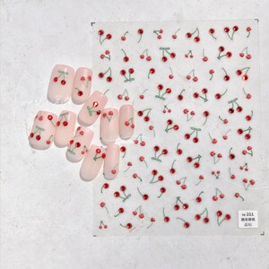 Pu&ograve; includere: Un foglio di adesivi per unghie con un design di ciliegie rosse con steli e foglie verdi. Gli adesivi sono su uno sfondo trasparente e hanno una finitura lucida. Il foglio include anche piccoli strass rossi.