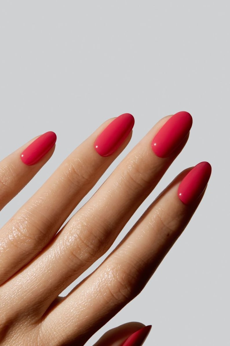 May include: Fingernails with a glossy, vibrant hot pink nail polish. The nails are shaped in a smooth, rounded oval style, showcasing a consistent, opaque, and reflective finish across all visible fingers against a neutral background.