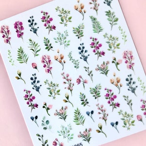 May include: A sheet of floral nail stickers with a variety of pink, white, and green flowers and leaves. The sheet has the product code DP1365 printed on it.
