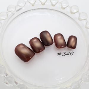 May include: Five press-on nails with a glossy, deep brown finish and a subtle metallic sheen. The nails are arranged in a row, featuring a rounded square shape. The text #349 is printed in black near the smallest nail on the right side.