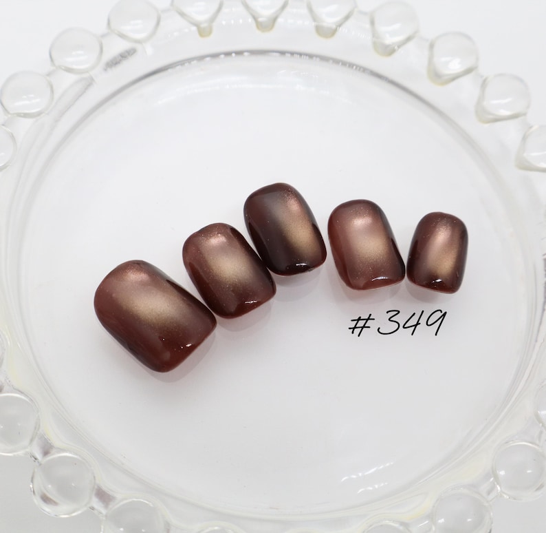 May include: Five press-on nails with a glossy, deep brown finish and a subtle metallic sheen. The nails are arranged in a row, featuring a rounded square shape. The text #349 is printed in black near the smallest nail on the right side.