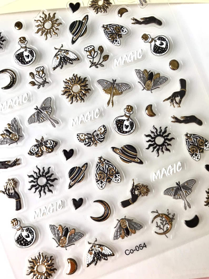 May include: A sheet of clear stickers with a variety of black and gold designs, including moons, stars, butterflies, planets, hands, and the word "MAGIC".