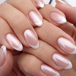 Op de afbeelding: Een klassieke French manicure met lange, ovaalvormige nagels met een natuurlijke roze basis en strakke witte randen. De glanzende afwerking benadrukt de gladde, afgeronde randen van elke nagel, wat zorgt voor een verzorgde en nette uitstraling.