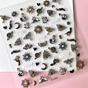 May include: A sheet of clear sticker paper with gold and black illustrations of moons, stars, planets, butterflies, and hands. The word "MAGIC" is repeated several times on the sheet. The sheet is labeled "CO-054".