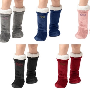 May include: Six pairs of plush, fleece boot socks with a sherpa lining. Each pair features a different colour and a name embroidered on the front:  Kila, Finn, Rose, Riley, Ava, and a sixth pair with an unreadable name.