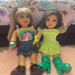 Pode incluir: Duas bonecas s&atilde;o exibidas, cada uma com cabelos longos e tra&ccedil;os faciais detalhados. Uma boneca usa um top tie-dye, uma saia jeans e sapatos pretos. A outra boneca est&aacute; em um vestido e botas verdes. Os acess&oacute;rios incluem pulseiras e uma x&iacute;cara pequena.