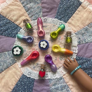 Pode incluir: Uma variedade de cachimbos pequenos pintados &agrave; m&atilde;o e potes decorativos com rolhas de corti&ccedil;a. Os cachimbos s&atilde;o de v&aacute;rias cores, incluindo rosa, verde e roxo. Os potes cont&ecirc;m rostos sorridentes e um cora&ccedil;&atilde;o vermelho. Dispostos sobre um edredom com estampa floral.