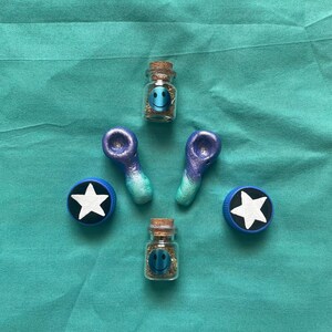 Pode incluir: Uma variedade de pequenos frascos de vidro com rolhas, cada um contendo um rosto sorridente e uma subst&acirc;ncia. Tamb&eacute;m est&atilde;o presentes dois cachimbos azuis e roxos e duas tampas de garrafa azuis com estrelas brancas. Os itens est&atilde;o dispostos em uma superf&iacute;cie azul-turquesa.