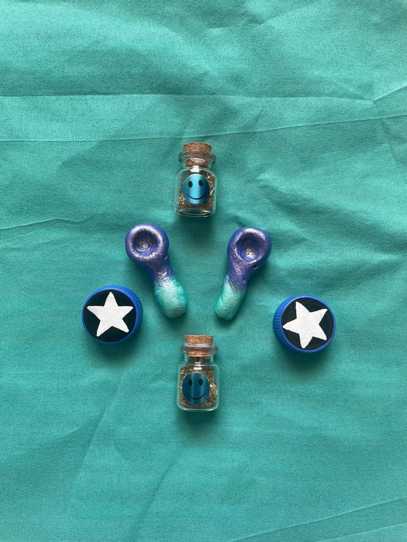 Pode incluir: Uma variedade de pequenos frascos de vidro com rolhas, cada um contendo um rosto sorridente e uma subst&acirc;ncia. Tamb&eacute;m est&atilde;o presentes dois cachimbos azuis e roxos e duas tampas de garrafa azuis com estrelas brancas. Os itens est&atilde;o dispostos em uma superf&iacute;cie azul-turquesa.