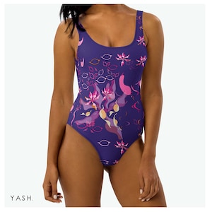 Puede incluir: Un bañador de una pieza de color índigo oscuro, adornado con un estampado floral en tonos rosa, morado y melocotón. El diseño presenta flores estilizadas y formas de hojas. La marca "YASH" está impresa en blanco en la parte inferior izquierda.