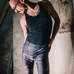 Peut inclure: Un débardeur noir associé à un pantalon à motifs. Le pantalon présente un motif quadrillé avec des silhouettes d'animaux orange. La tenue est portée dans un cadre rustique et faiblement éclairé.