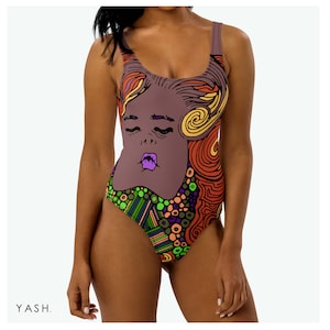 Puede incluir: Un bañador de una pieza con un diseño abstracto colorido que presenta la cara de una mujer. El diseño incluye remolinos, puntos y formas geométricas en tonos de verde, naranja, morado y marrón.