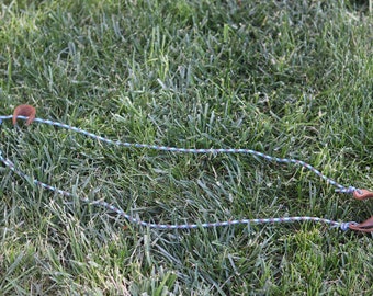 May include: A blue and brown braided rope with leather loops at each end. The rope is lying on a bed of green grass.