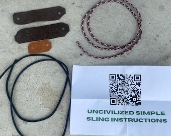 May include: An assortment of sling-making components, including leather pieces, a braided cord in red, white, and black, and a black cord. A white paper with the text "UNCIVILIZED SIMPLE SLING INSTRUCTIONS" and a QR code is also present.