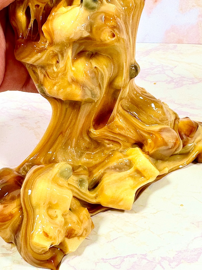 May include: Close-up of a brown and yellow slime with a swirled pattern. The slime is being stretched and pulled, revealing its gooey texture.