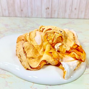Puede incluir: Primer plano de una sustancia blanca y pegajosa con una cobertura marr&oacute;n de caramelo. La cobertura est&aacute; en espiral y tiene un aspecto ligeramente derretido.