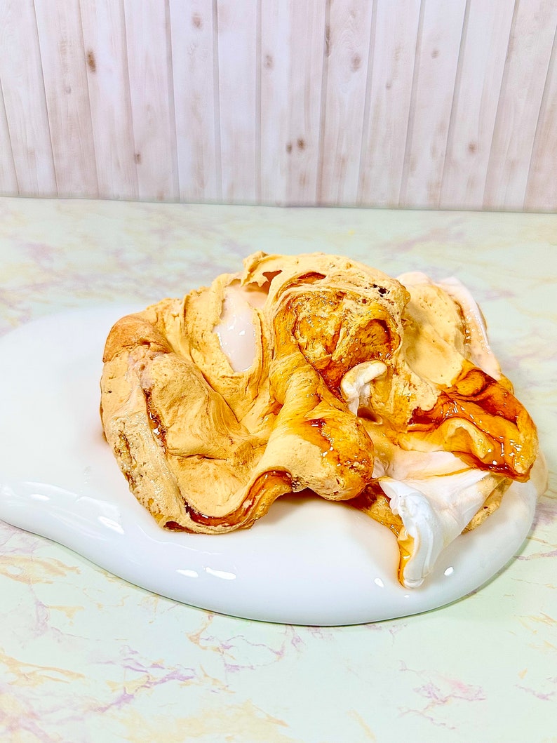 Puede incluir: Primer plano de una sustancia blanca y pegajosa con una cobertura marr&oacute;n de caramelo. La cobertura est&aacute; en espiral y tiene un aspecto ligeramente derretido.