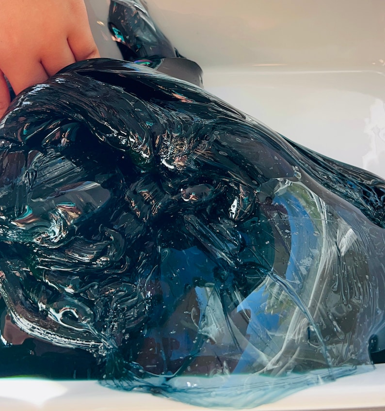 May include: A large amount of dark blue slime in a white container. The slime is very thick and gooey, and it has a slightly iridescent sheen.