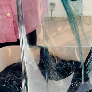 May include: A person is holding a clear plastic sheet over a container of dark blue slime. The slime is thick and gooey, and it is filling the container.